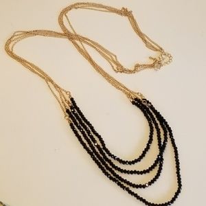 Long multistrand black beaded necklace with gold chains.